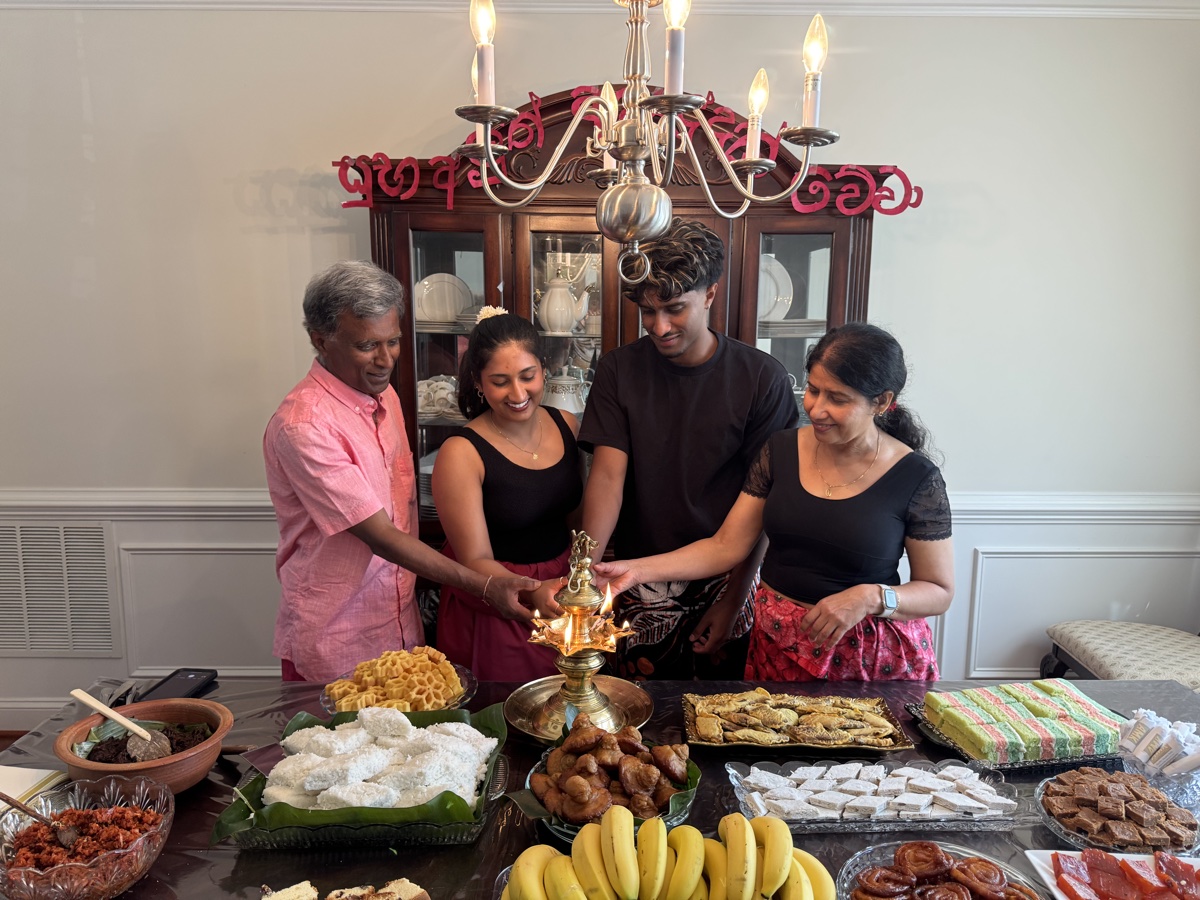 Priyanthi and her family lighting a traditional brass oil lamp over a table of Sri Lankan sweets